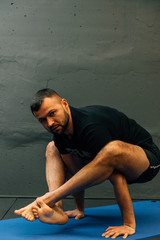 Obraz premium Sporty young man working out, doing handstand yoga. Studio shot in urban fitness gym with grey background for copy space.