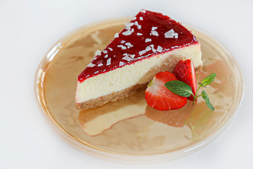 Delicious healthy vegetarian food, organic strawberry cheesecake slice, fresh red berries, green mint leaves on beautiful glass plate. White wood texture table background. Close up, top front view.