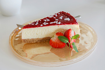 Delicious healthy vegetarian food, organic strawberry cheesecake slice, fresh red berries, green mint leaves on beautiful glass plate. White wood texture table background. Close up, top front view.