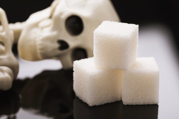Three pieces of sugar and a human skeleton, close-up. Concept on the topic of harmful products