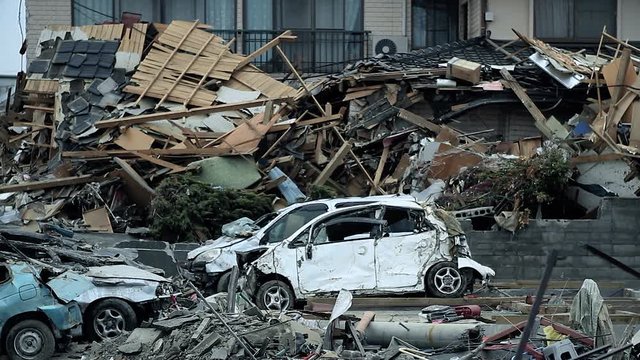 There is a lot of ruins of the city and houses. Destroyed cars are everywhere after the tsunami of Fukushima in 2011