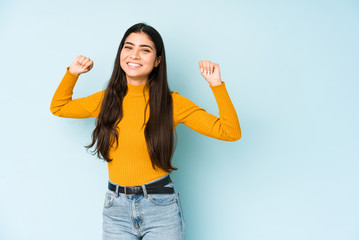Young indian woman isolated on blue background celebrating a special day, jumps and raise arms with energy.