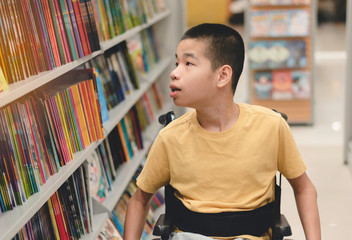 Disabled child on wheelchair having fun choosing books from shelves, Special children's lifestyle, Life in the education age of special need kids, Happy disability kid concept, Selective focus.