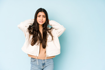 Young indian woman on blue background touching back of head, thinking and making a choice.