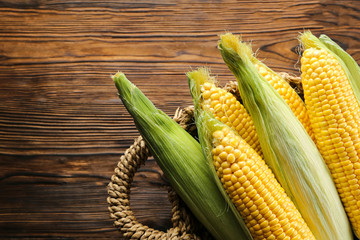 Cobs of ripe raw corn laid on dark wood textured table. Healthy summer food concept. Fresh uncooked corncob. Clean eating habits. Background, top view, close up, flat lay, copy space.