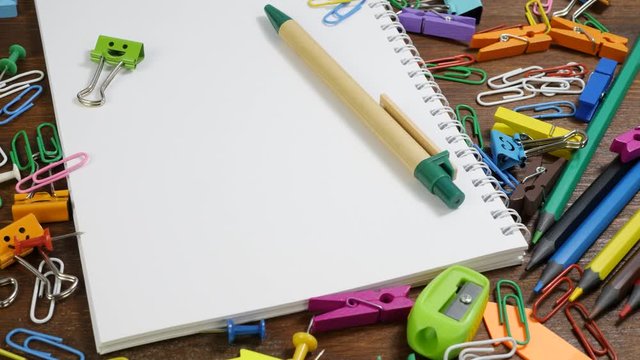 School paper notebook and various stationery on brown wooden Table. Multi-colored pencils, paper clips, chips, smiles binder clips. Concept of back to school, education or knowledge