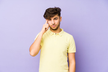 Young arabian man isolated on a purple background pointing temple with finger, thinking, focused on a task.