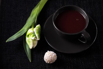 Black Cup with hot chocolate and white candy on the table. A white Tulip is lying next to the Cup.