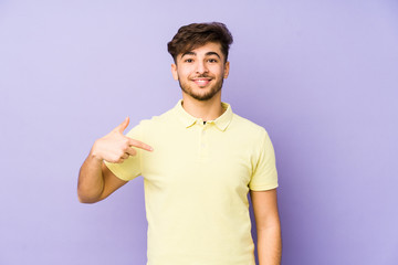 Young arabian man isolated on a purple background person pointing by hand to a shirt copy space, proud and confident