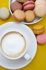 Cup of coffee and macaroons on colorfu lyellow background. top view.