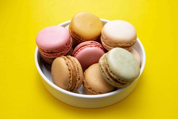 Colorful macaroons cookies dessert on a plate, with yellow background.