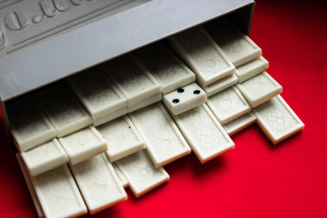 Domino Bones of dominoes fell out of a gray case on a red fabric background and a lot of space for text. The reverse side of dominoes. On the cover of the case is the inscription "Domino"
