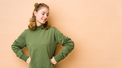 Young caucasian woman isolated on beige background laughs happily and has fun keeping hands on...