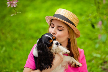 Close- up portrait of a dog owner kissing a small cavalier king Charles Spaniel in a Park in the spring. Young blonde, having fun with her dog.