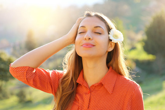 Spring girl. Close up portrait of beautiful relaxed young woman with white flower on ear breathing fresh air with closed eyes outdoor in spring time.
