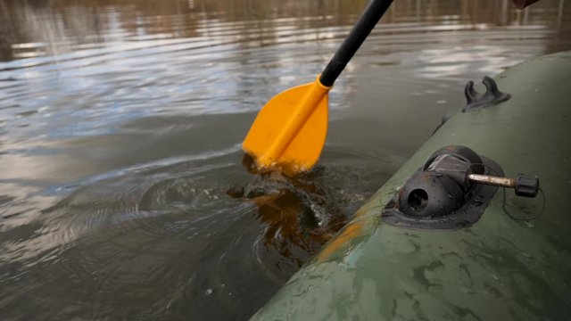 Close up of a man on a river in a green rubber boat with a yellow paddle. Stock footage. Male rowing with an oar sitting in a rubber boat.