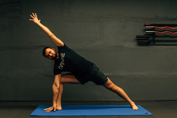 Middle aged attractive man practicing yoga concept, sitting in difficult pose, working out wearing black sportswear. Healthy lifestyle concept.