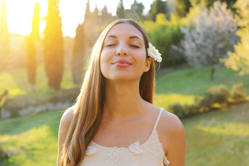 Portrait of young smiling woman with closed eyes and flower on ear taking deep breathing. Positive spring girl emotion face expression feeling life perception success peace mind concept. 