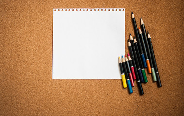 various colored pencils on cork Board background with white sheet of paper