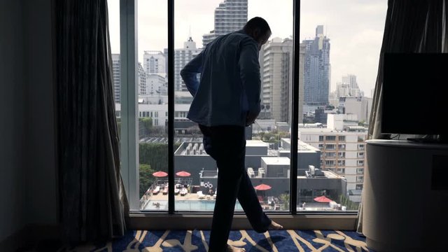 Young businessman putting on trousers by window at hotel room