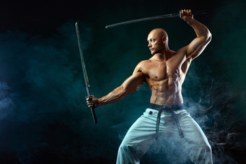 Karate fighter on black background with smoke. Shirtless man samurai with Japanese sword. Fit man...