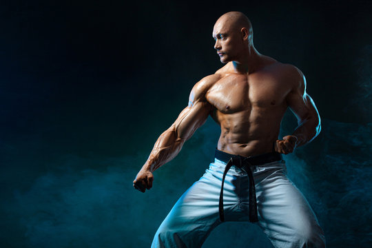 Karate or taekwondo fighter on black background with smoke. Fit man sportsmen bodybuilder physique and athlete. Men's sport motivation. - Powered by Adobe