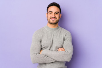 Young caucasian man isolated on purple background who feels confident, crossing arms with determination.