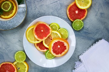 Assorted colors of citrus slices on a white plate against a gray textured background