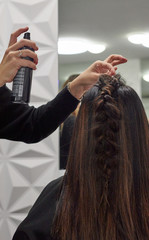Naklejka premium Hairdresser makes braid and puts hairspray