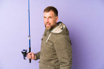 Senior fisherman isolated on purple background looks aside smiling, cheerful and pleasant.