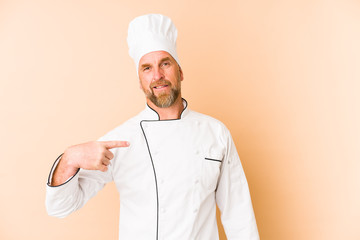 Chef man isolated on beige background person pointing by hand to a shirt copy space, proud and confident