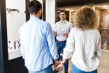 Obraz premium Couple at interior decor store talking with seller manager about tab bath trying to choose the right ones