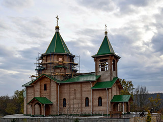Fototapeta na wymiar Wooden Orthodox church under construction with green roof and gilded crosses.