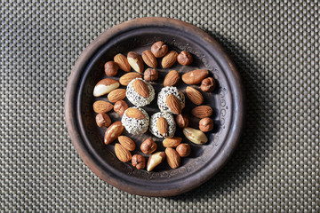 Various nuts are laid out in a brown handmade clay plate.