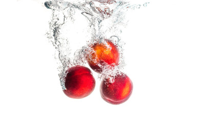 Fototapeta na wymiar Nectarine fruits splashing into water and sinking with air bubbles isolated on white background