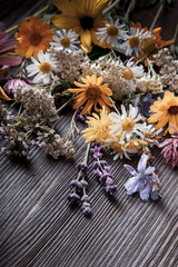 Fototapeta premium Flowers on old grunge wooden table (chamomile lupine dandelions thyme mint bells rape). Wild nature background