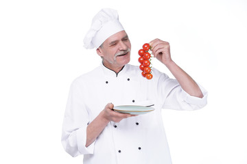Professional chef in white uniform and hat, holding plate with tomatoes on white background