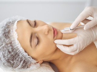 Obraz na płótnie Canvas Beautician doing beauty procedure with syringe to face of young brunette woman. Cosmetic medicine and surgery, beauty injections