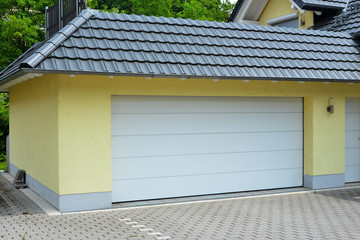 Garage mit Automatik-Rolltor und grauem Ziegeldach angebaut an ein modernes Einfamilienhaus