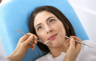 Smiling brunette woman being examined by dentist at dental clinic. Hands of a doctor holding dental instruments near patient's mouth. Healthy teeth and medicine concept