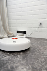White robot vacuum clesaner on a gray floor. Modern mart floor cleaning device.