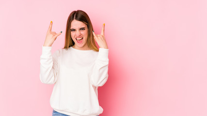 Young caucasian woman isolated on pink background showing a horns gesture as a revolution concept.