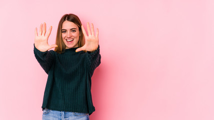 Young caucasian woman isolated on pink background showing number ten with hands.