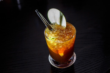 A cocktail with whiskey or cognac or Cola in a highball glass is on the counter of a dark bar.