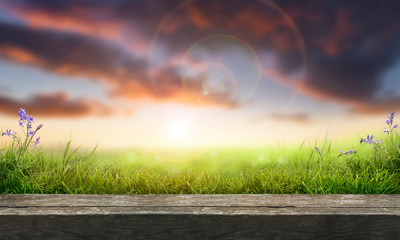 A wooden table top product display with a sunny summer sunset background with a fresh green grass foreground.