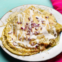 Mexican green enchiladas with melted cheese on turquoise background