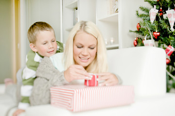 Obraz na płótnie Canvas Happy woman with child opening Christmas gift and enjoying Christmas atmosphere