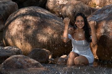 Fototapeta na wymiar Joven morena de pelo sentado en una roca en las montañas jugando con agua y salpicaduras.