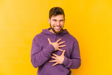 Young caucasian man isolated on yellow background laughs happily and has fun keeping hands on...