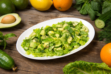 Green salad with citrus vinaigrette, avocado cucumber green beans and romaine salad in an oval dish on a rustic wooden table. Selected focus.